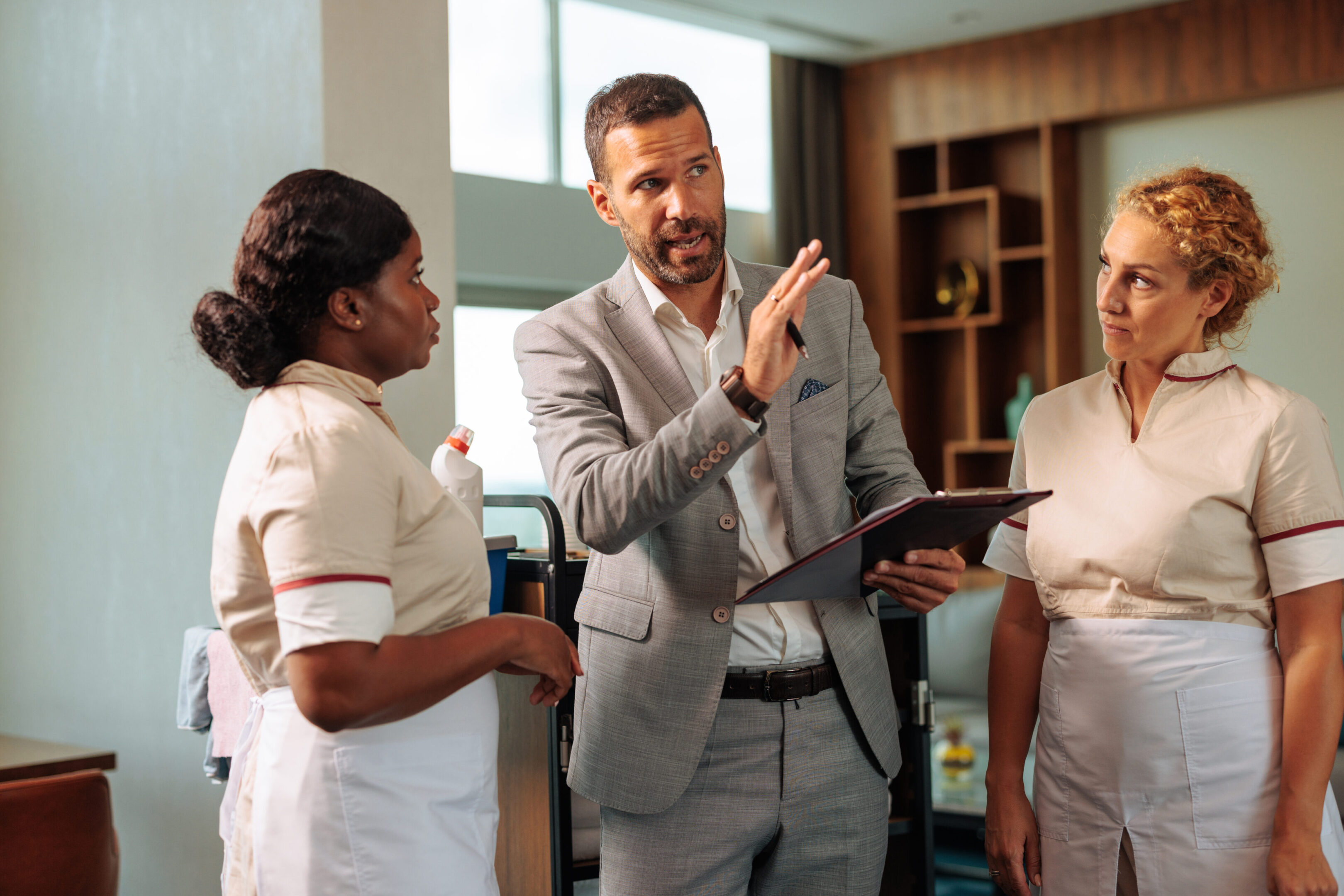 Shift manager in grey suit explaining the procedure to two diverse housekeepers
